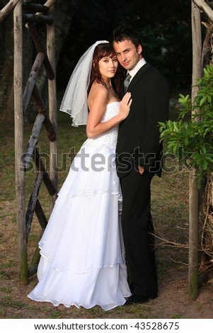 stock photo Handsome wedding couple standing under a wooden arch outdoors