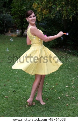 Gorgeous brunette girl in yellow dress twirling round an blowing soap bubbles