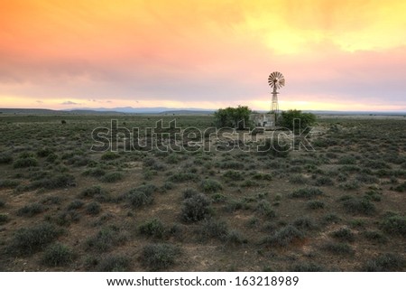 Wide open farm land with a water windmill pump at sunset in the Karoo in South Africa