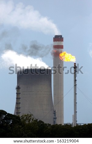 Energy production plant with cooling towers, chimneys and gas flame