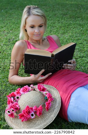 Pretty young woman reclining on the grass while reading a book