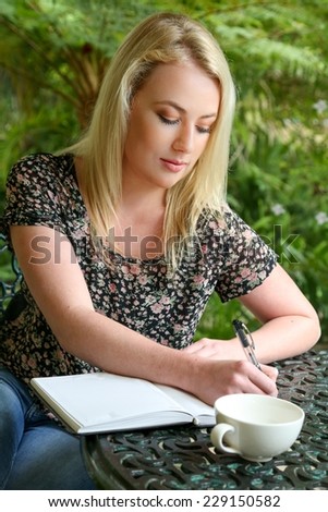 Lovely blond woman writing in her journal while sitting at a table outdoors