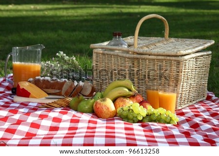 Sumptuous picnic spread out on a red and white checked cloth with wicker basket