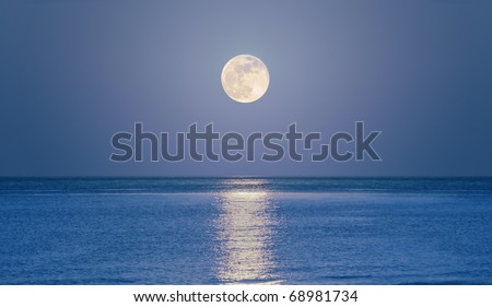 Big full moon is rising above the sea at dusk.