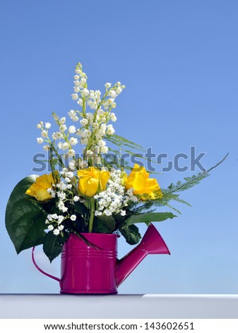 Spring bunch with roses and lilies of the valley in watering can, blue sky background.
