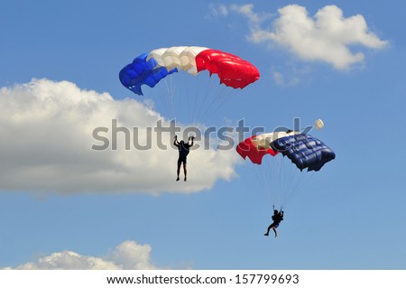 Two parachutes on blue sky with white clouds.