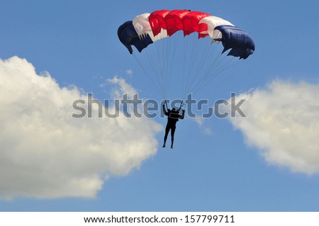 Blue white and red sail parachute on blue sky with white clouds.