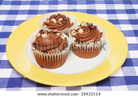 Three chocolate cup cakes on plate and table cloth
