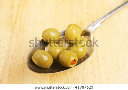 Olives in a silver serving spoon on a wooden board