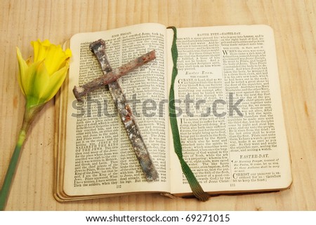 Antique prayer book open to Easter prayers with a cross of iron nails and a daffodil flower on a background of wood