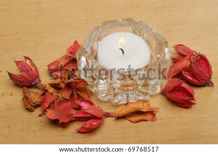 Tea light candle in a crystal glass holder with potpourri on a wooden board