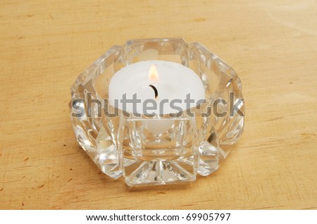 Tea light candle with burning flame in a cut crystal glass holder on a background of weathered wood