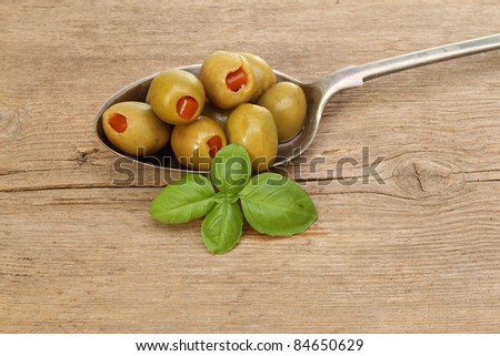 Stuffed olives in silver spoon with a sprig of basil on old rustic wood