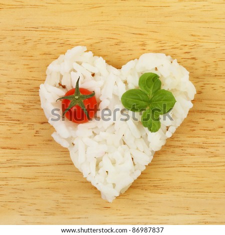 Healthy food, rice in a heart shape with tomato and basil on a wooden board