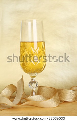 Glass of champagne and a gold ribbon against a gold background