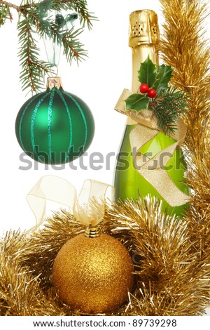 Christmas theme,bottle of champagne decorated with holly, pine needles and a gold ribbon bow surrounded by tinsel and gold glitter bauble and a green bauble hanging from a Christmas tree