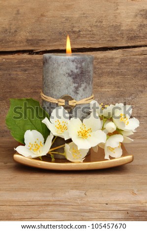 Burning Feng Shui candle and white philadelphus flowers on a gold dish against a background of weathered wood
