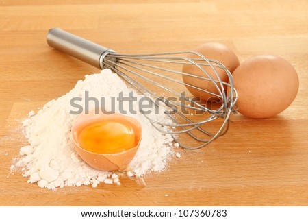 Closeup of flour cracked and whole eggs with a whisk on a wooden worktop