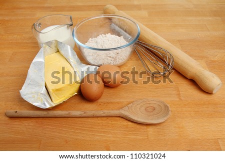 Baking ingredients, flour,eggs,milk and margarine with a whisk,wooden spoon and a rolling pin on a wooden worktop