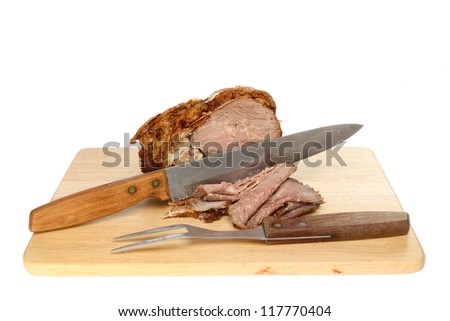 Roast beef with a carving knife and fork on a wooden board isolated against white