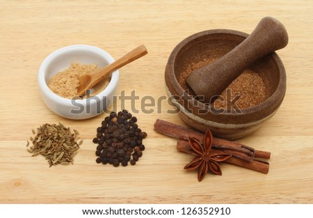 Ingredients for Chinese five spice with a ramekin and pestle and mortar on a wooden board