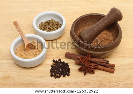 Ingredients for Chinese five spice with ramekins and a pestle and mortar on a wooden board