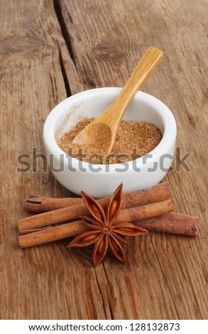 Chinese five spice in a ramekin with star anise and cinnamon sticks on a background of old weathered wood