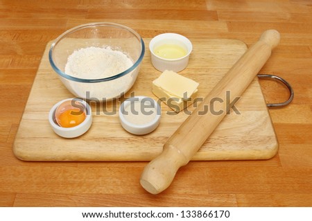 Pastry ingredients and rolling pin on a wooden board on a kitchen worktop