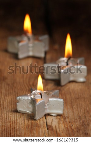 Burning silver star shaped candle with two others behind in soft focus on old weathered wood