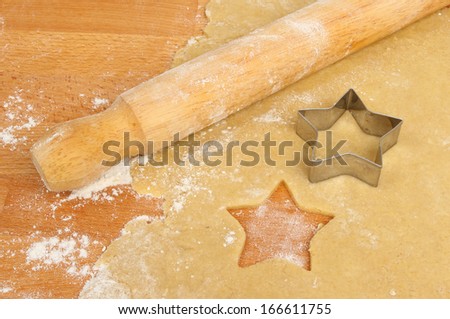 Christmas star pastry cutter on rolled sweet pastry with a rolling pin on a floured wooden board