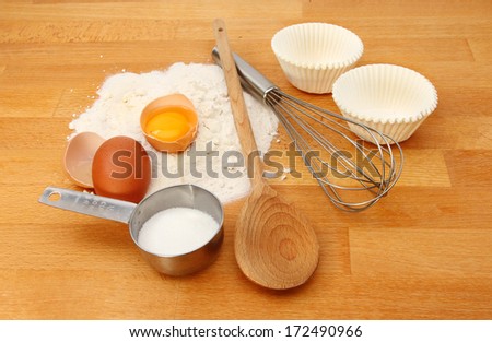 Muffin ingredients on a wooden kitchen worktop, flour, eggs,sugar, muffin cases and utensils