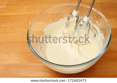 Cake mix in a glass mixing bowl with a whisk on a wooden worktop