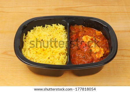 Convenience meal of chicken curry and rice in a plastic carton on a wooden worktop