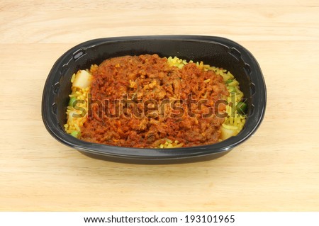 Convenience meal, lamb biryani, in a plastic tray on a wooden tabletop
