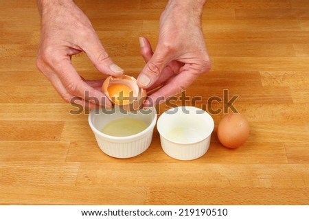 Hands separating egg yolks into ramekins on a wooden worktop