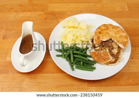 Meal on a tabletop, chicken pie potatoes and beans with gravy in a gravy boat