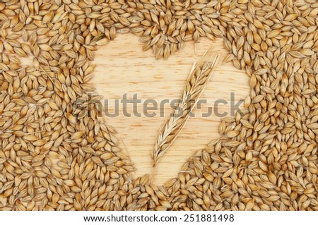 Grains of barley on a wooden board with a heart shaped space with an ear of barley