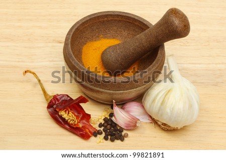 Pestle and mortar with, chilli,pepper,garlic and tumeric on a wooden board