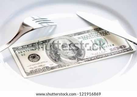 Big bucks/ One hundred american dollars bill on a white plate, with fork and knife. Buying power, money management, charity events & other in business, economy, finance, banking and everyday life.