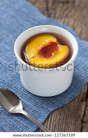 Appetizing serving of canned peaches in syrup. White bowl on blue table mat on a rustic wooden table.