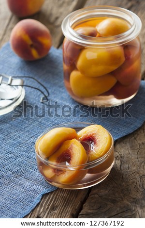 Canned peaches: serving bowl next to a jar and fresh fruits. Blue table mat on a rustic wooden table.