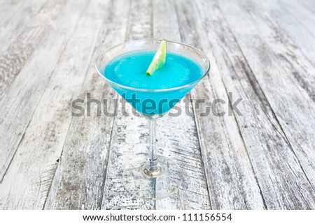 Frozen Blue Margarita Cocktail in martini glass with lemon isolated on wood table