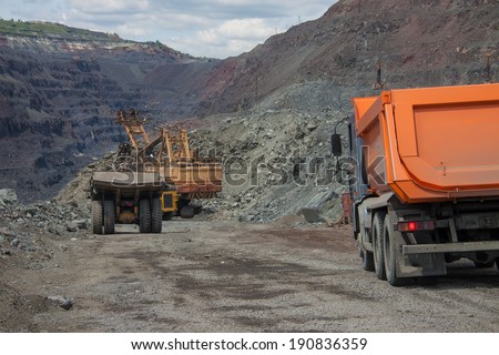 Heavy mining trucks being loaded with iron ore on the opencast