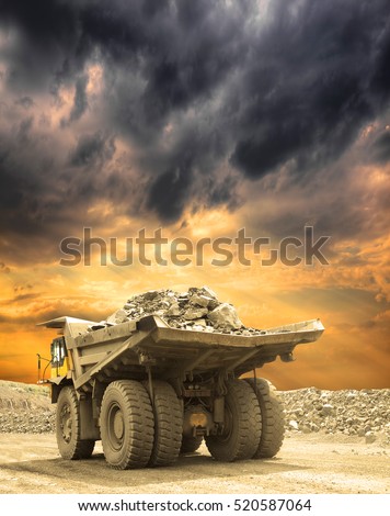 Heavy mining truck loaded with iron ore driving along the opencast on a stormy sunset