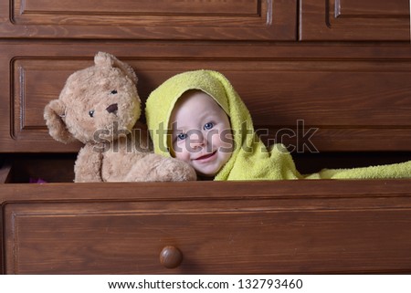 cute baby with bear peeks out of the drawer cabinet