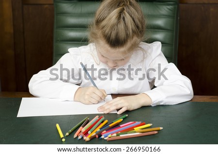 Portrait of preschooler girl drawing with pencils and thinking about it. Sitting in a green leather armchair, at the dark table