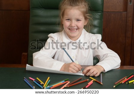 Portrait of preschooler girl drawing with pencils and thinking about it. Sitting in a green leather armchair, at the dark table