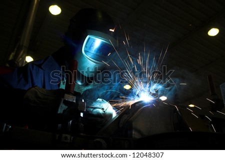 Welder welding a metal part in an industrial environment, wearing standard protection equipment. Sparks flying, fumes, industrial background