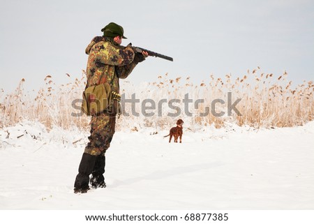 Hunter aiming at the prey, dog waiting for the shotgun to fire. Hunting winter open season scene