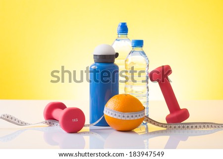 Body building dumbells,water, sport bottle and orange wrapped with white measuring tape, fitness
